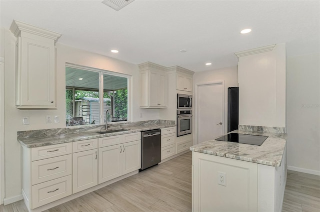 kitchen featuring light wood-style floors, light stone counters, black appliances, white cabinetry, and a sink