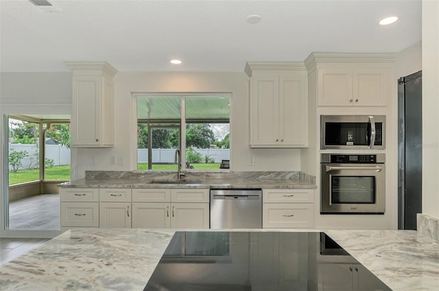 kitchen with stainless steel appliances, light stone counters, a sink, and white cabinets