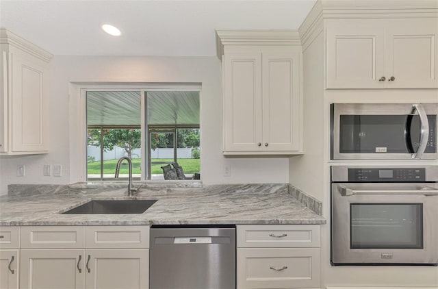 kitchen featuring recessed lighting, stainless steel appliances, a sink, white cabinets, and light stone countertops