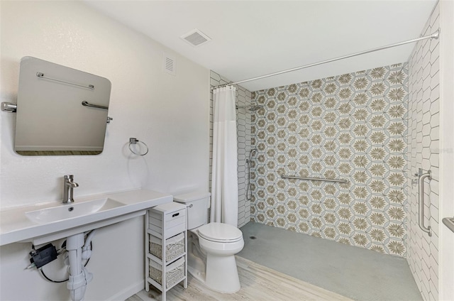 bathroom featuring visible vents, tiled shower, toilet, wood finished floors, and a sink