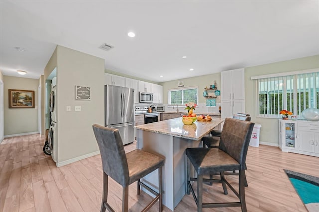 kitchen with a breakfast bar area, stacked washer / drying machine, visible vents, appliances with stainless steel finishes, and white cabinets