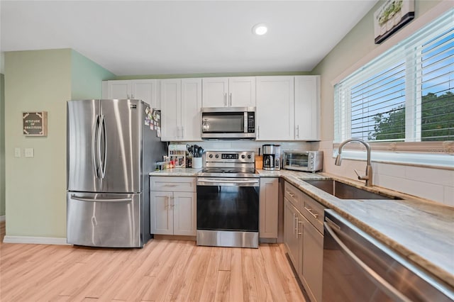 kitchen with a toaster, appliances with stainless steel finishes, light stone counters, light wood-style floors, and a sink