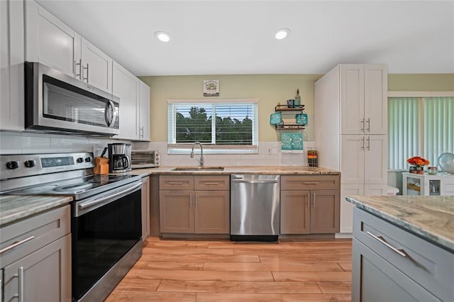 kitchen with light wood finished floors, light stone counters, a sink, stainless steel appliances, and backsplash