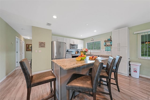 kitchen featuring a center island, visible vents, appliances with stainless steel finishes, white cabinetry, and a kitchen bar