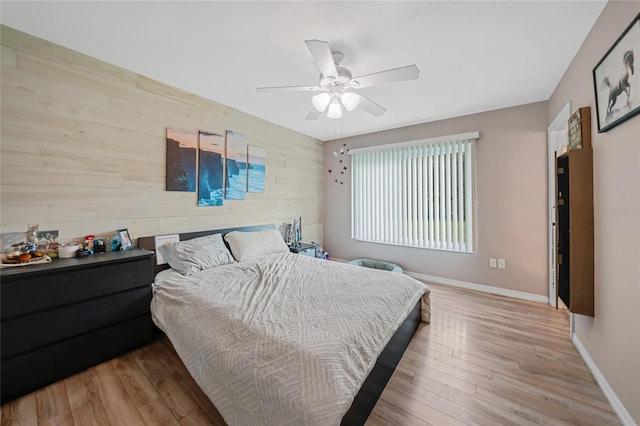 bedroom featuring wood walls, an accent wall, baseboards, and wood finished floors