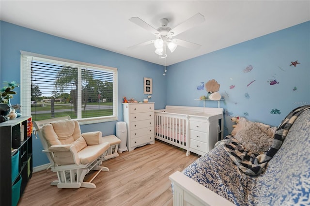 bedroom featuring a ceiling fan, light wood-type flooring, and a crib