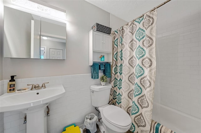 bathroom featuring a textured ceiling, toilet, shower / tub combo, tile walls, and wainscoting