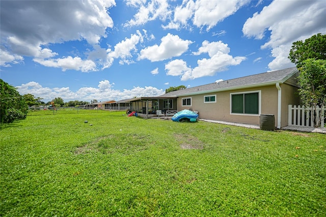 rear view of house featuring fence, a lawn, and stucco siding