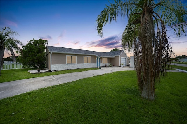 view of front of property with concrete driveway, a lawn, fence, and stucco siding