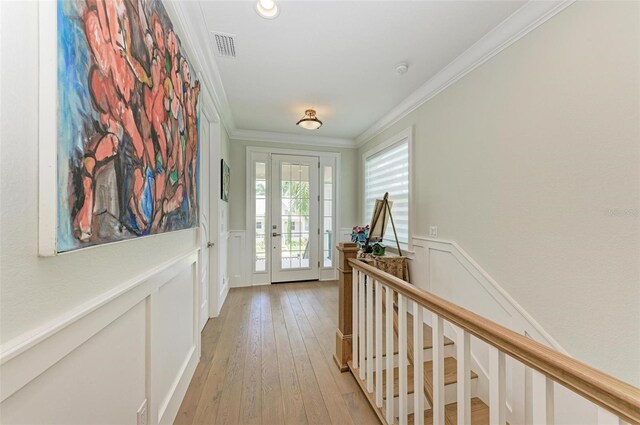 entryway featuring light wood-type flooring, a wainscoted wall, crown molding, and visible vents