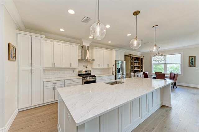 kitchen featuring hanging light fixtures, wall chimney exhaust hood, stainless steel gas range oven, and a large island with sink