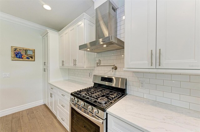 kitchen with stainless steel gas range oven, white cabinets, wall chimney exhaust hood, light wood-style flooring, and light stone counters