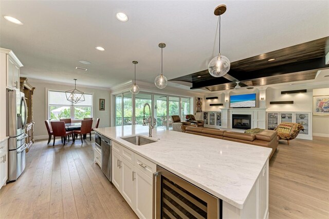 kitchen featuring an island with sink, beverage cooler, white cabinetry, and a sink