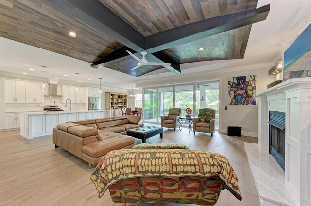 living room with beam ceiling, ornamental molding, a high end fireplace, light wood-type flooring, and baseboards