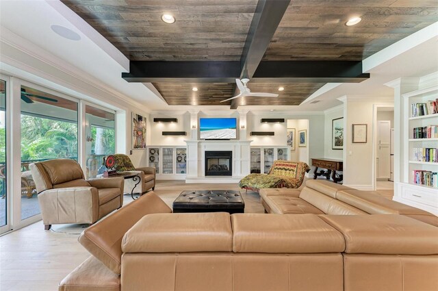 living area with a fireplace with raised hearth, light wood-style flooring, a ceiling fan, ornamental molding, and beamed ceiling