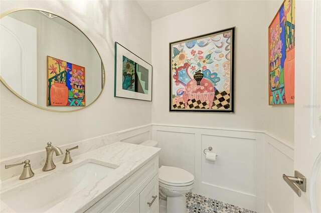 bathroom with a wainscoted wall, a decorative wall, vanity, and toilet