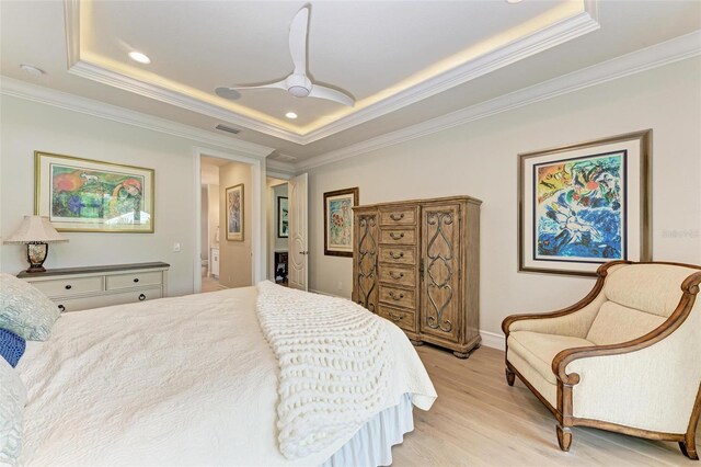 bedroom with light wood finished floors, a tray ceiling, visible vents, and crown molding