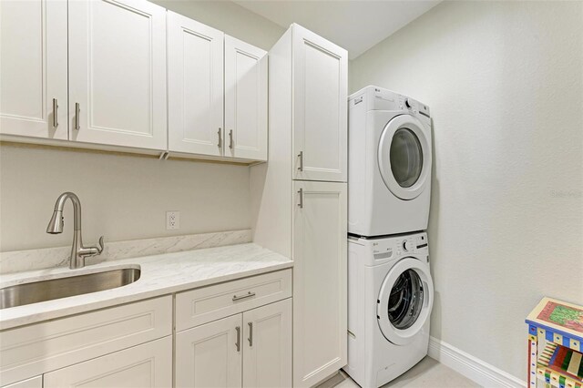 laundry area featuring stacked washer and dryer, cabinet space, baseboards, and a sink