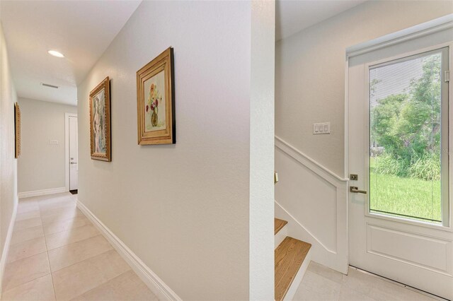 corridor featuring stairs, light tile patterned flooring, baseboards, and a healthy amount of sunlight