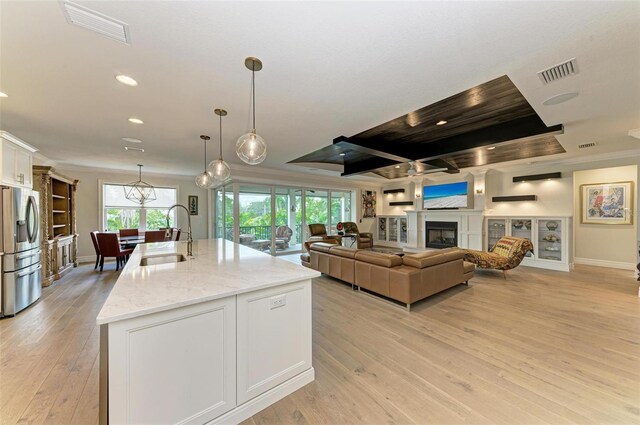 kitchen featuring visible vents, white cabinets, stainless steel fridge with ice dispenser, an island with sink, and light stone countertops