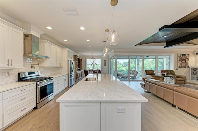 kitchen with wall chimney exhaust hood, a center island with sink, stainless steel appliances, and a sink