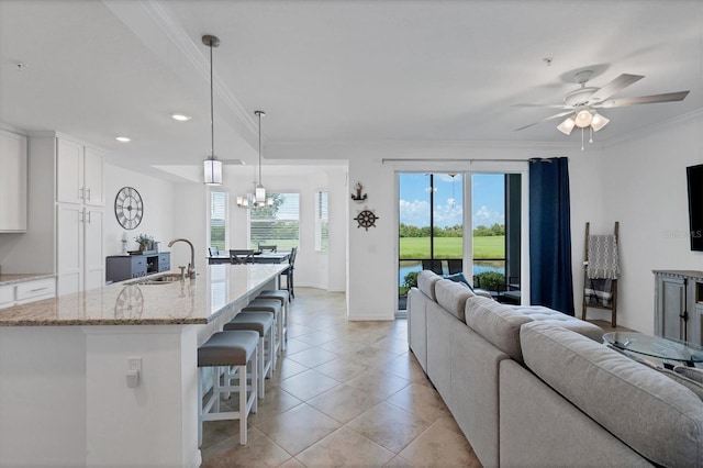 living room featuring light tile patterned flooring, ceiling fan with notable chandelier, crown molding, and sink