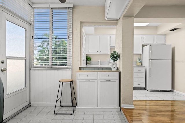 kitchen featuring light tile patterned floors, white refrigerator, and white cabinetry