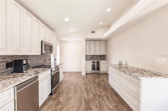 kitchen featuring hardwood / wood-style floors, backsplash, beverage cooler, light stone countertops, and appliances with stainless steel finishes