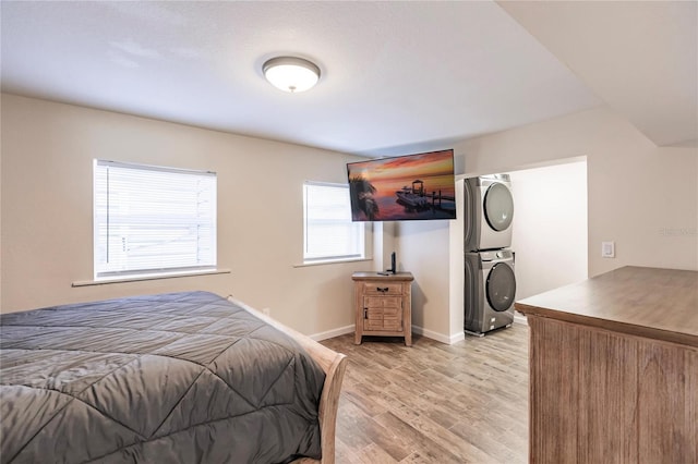 bedroom featuring baseboards, light wood finished floors, and stacked washer / drying machine