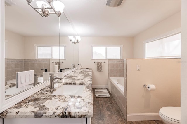 bathroom featuring tiled bath, visible vents, toilet, wood finished floors, and a notable chandelier