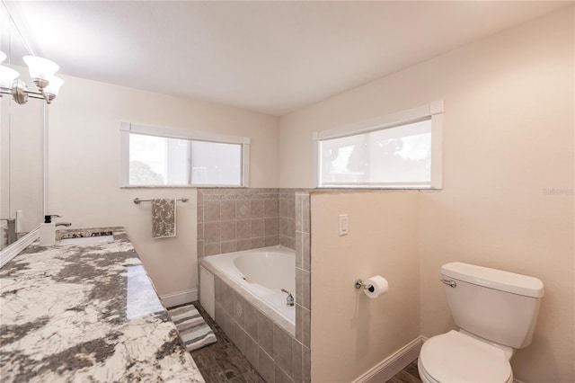 bathroom with tiled tub, toilet, hardwood / wood-style floors, and a healthy amount of sunlight