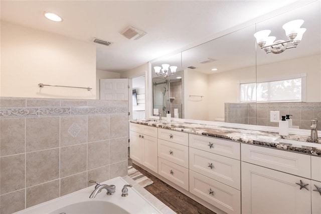 full bath with tile walls, double vanity, visible vents, an inviting chandelier, and a sink