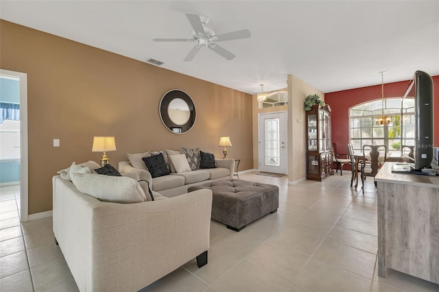 living area featuring ceiling fan with notable chandelier, baseboards, visible vents, and light tile patterned floors