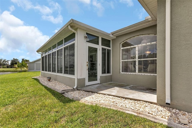 rear view of property with a patio area, a lawn, a sunroom, and stucco siding
