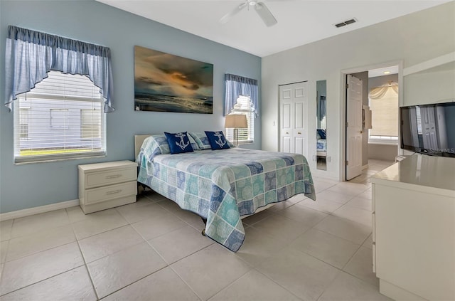 tiled bedroom with multiple windows, ceiling fan, and ensuite bath