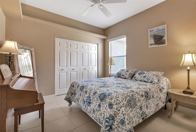 bedroom with a textured wall, light tile patterned floors, a closet, baseboards, and ceiling fan
