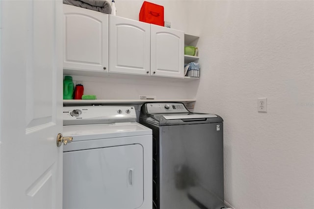 laundry room with separate washer and dryer, a textured wall, and cabinet space