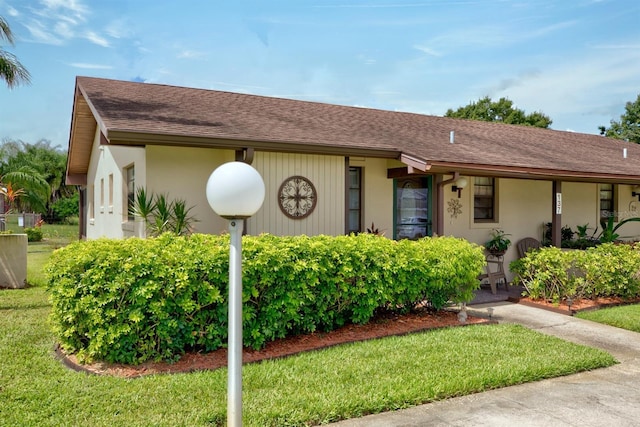 single story home with a shingled roof, a front lawn, and stucco siding