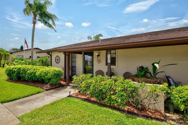 ranch-style house with stucco siding, roof with shingles, and a front yard