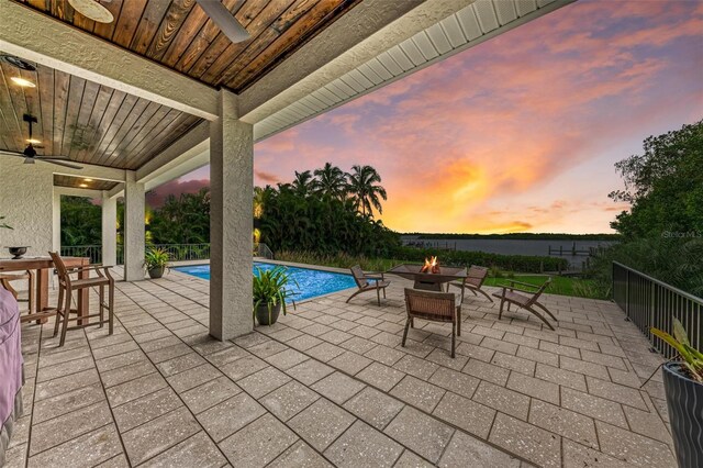 patio terrace at dusk with a fenced in pool and a fire pit