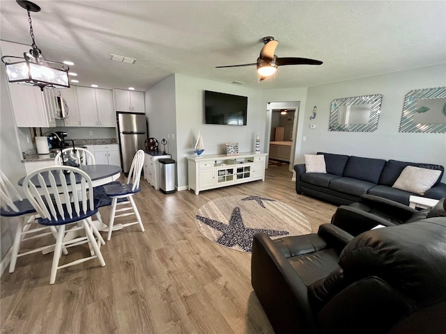 living room with light wood-type flooring, ceiling fan with notable chandelier, and a textured ceiling