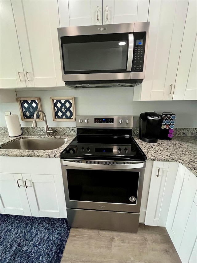 kitchen with appliances with stainless steel finishes, light stone counters, white cabinetry, and sink