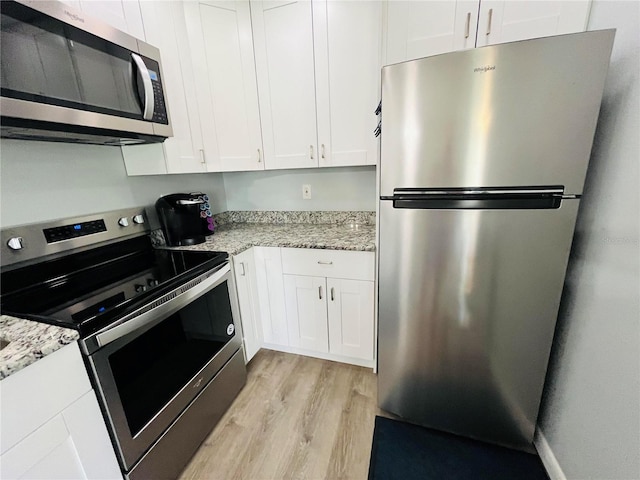 kitchen with light stone counters, light wood-type flooring, appliances with stainless steel finishes, and white cabinetry