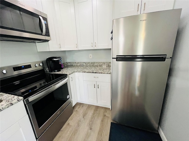 kitchen with light stone countertops, light wood-style floors, appliances with stainless steel finishes, and white cabinets