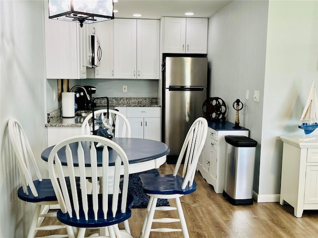 kitchen with baseboards, dark stone counters, appliances with stainless steel finishes, light wood-type flooring, and white cabinetry