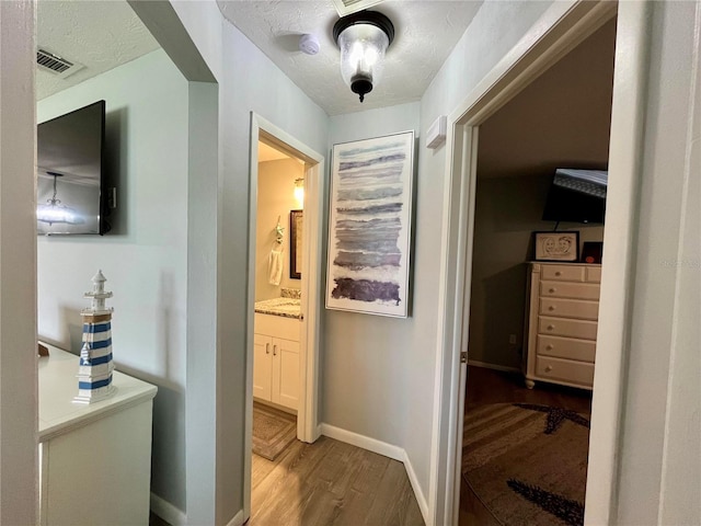 corridor featuring a textured ceiling, wood finished floors, visible vents, and baseboards