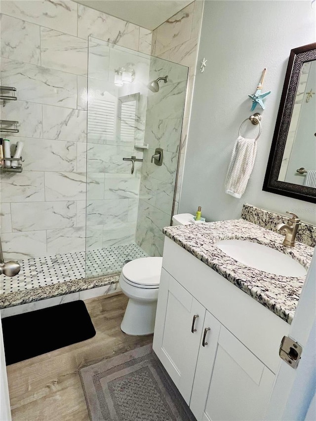 full bath with toilet, a marble finish shower, wood finished floors, and vanity