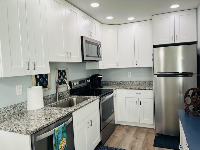 kitchen featuring light stone counters, light wood-style flooring, appliances with stainless steel finishes, white cabinetry, and a sink