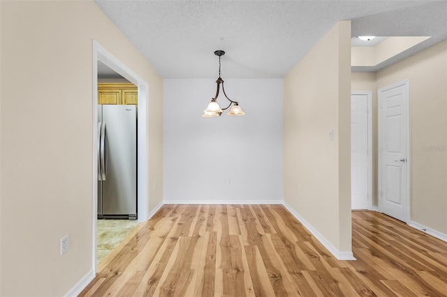 unfurnished dining area featuring a textured ceiling, light wood-type flooring, a notable chandelier, and baseboards