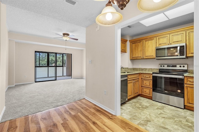 kitchen with light stone counters, appliances with stainless steel finishes, a textured ceiling, light colored carpet, and ceiling fan